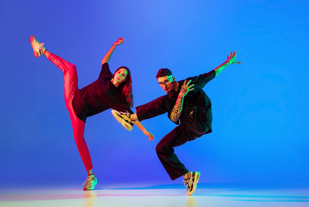 Zwei junge Leute, Mann und Frau tanzen Bremstanz, Hip-Hop vor blauem Hintergrund im Neonlicht. - Foto, Bild