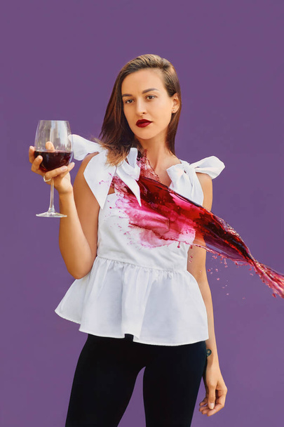 Nyugodt vonzó nő fehér blúzban, egy pohár vörösborral a kezében, vörösboros fröccsenéssel. Agresszió, nyugalom, ünneplés, borászat koncepció - Fotó, kép