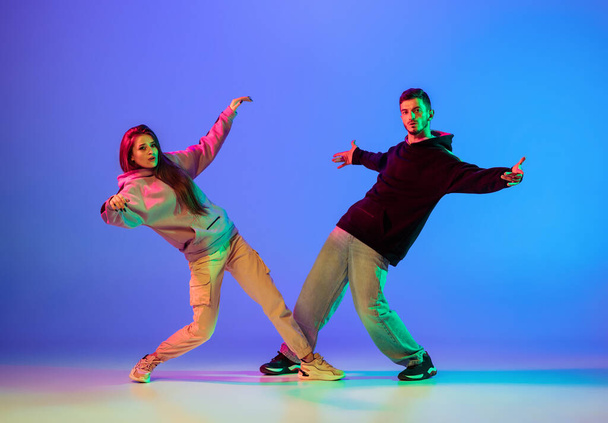 Dos jóvenes, hombre y mujer bailando frenado, hip-hop sobre fondo azul en luz de neón. - Foto, Imagen