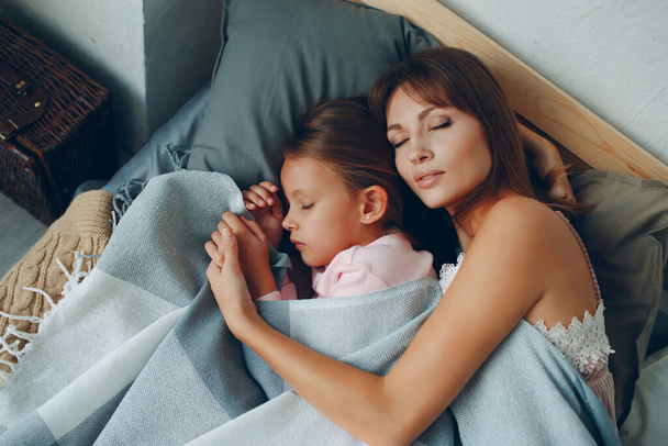 Anne küçük kızına sarılarak uyuyor. Aile ve anneler günü konsepti. - Fotoğraf, Görsel