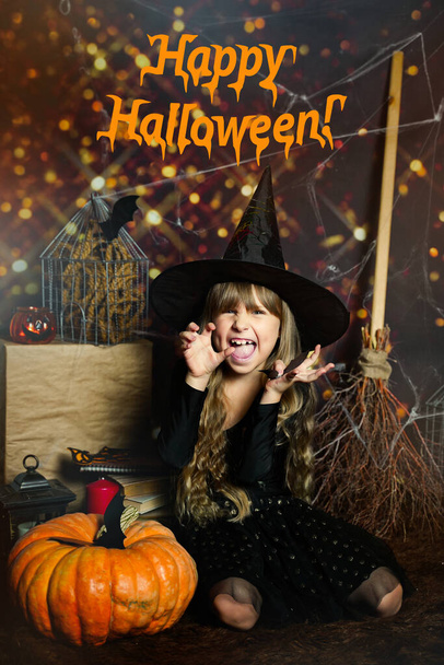 tekst gefeliciteerd Happy Halloween op de foto Preschool meisje schrikt, uitdrukking van emoties kwaad lachen in een heksen hoed met een pompoen  - Foto, afbeelding
