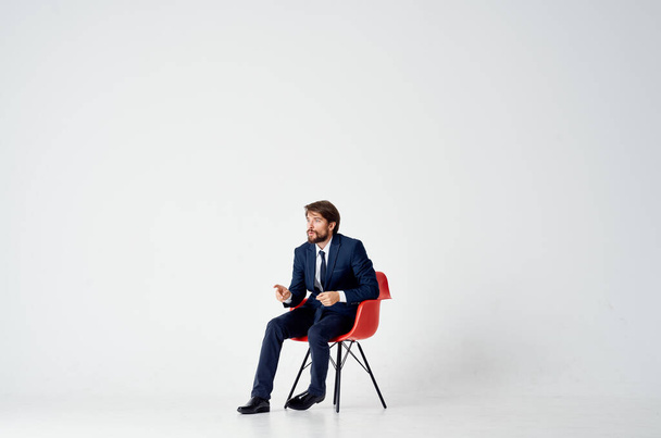 επιχειρηματίας με κοστούμι κάθεται σε κόκκινο καρέκλα συναισθήματα γραφείο - Φωτογραφία, εικόνα