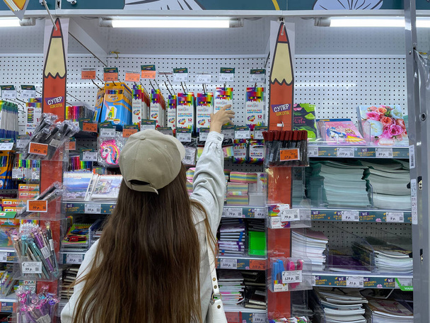 The girl reaches for the colored pencils on the top shelf. A schoolgirl buys a stationery for the new school year. Parents buy colored pencils for children. - Valokuva, kuva