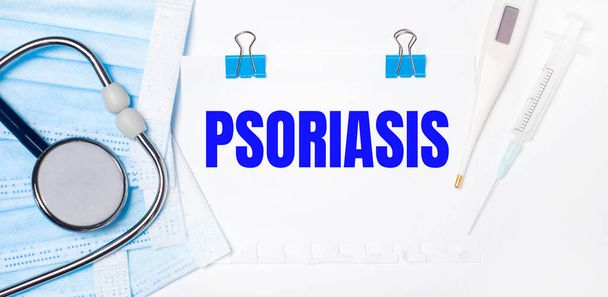 On a light background lie a stethoscope, an electronic thermometer, a syringe, a face mask and a sheet of paper with the text PSORIASIS. Medical concept - 写真・画像