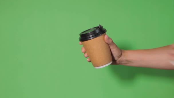 Yeşil arka planda yakın plan, bir kadının eli ayakta kahve olan bir kağıt bardağı tutuyor. Kahve ya da çay. İnsanlar birbirlerine kahve ve kahve dağıtırlar.. - Video, Çekim