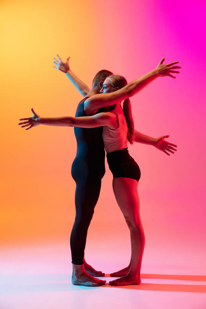 Two dancers, stylish sportive couple, male and female models dancing contemporary dance on colorful gradient yellow pink background in neon light. - Foto, Imagem