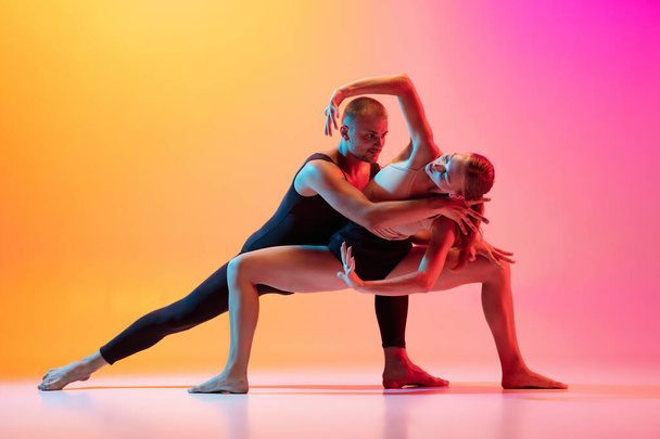 Two dancers, stylish sportive couple, male and female models dancing contemporary dance on colorful gradient yellow pink background in neon light. - Фото, зображення