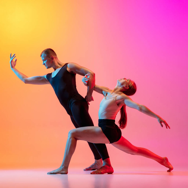 Two dancers, stylish sportive couple, male and female models dancing contemporary dance on colorful gradient yellow pink background in neon light. - Fotó, kép