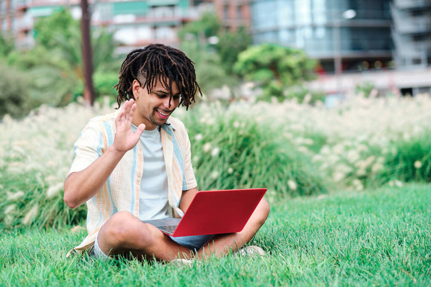 jeune homme latin aux cheveux bouclés dans une vidéoconférence au parc à l'aide d'un ordinateur portable - Photo, image