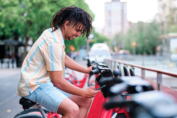 young latin man unlocking a bycicle for transportation - Fotó, kép