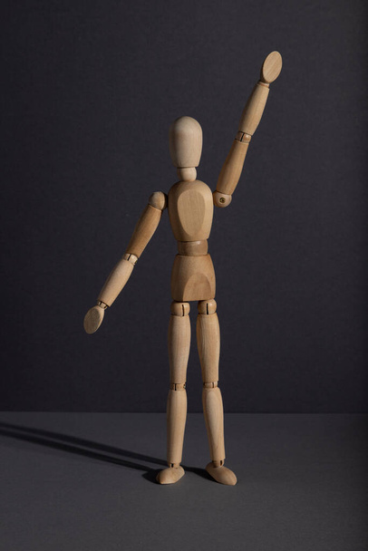 Wooden mannequin stands with raised hand on gray background. protest, attention concept. copy space, hard light. - 写真・画像