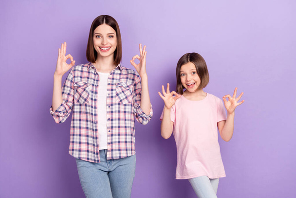Portrait of two attractive cheerful girls showing ok-sign ad advert isolated over purple violet color background - 写真・画像