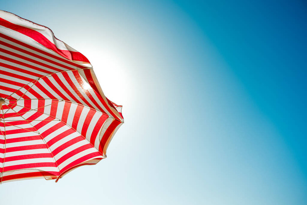 Red striped sun umbrella and blue sky. - Fotó, kép