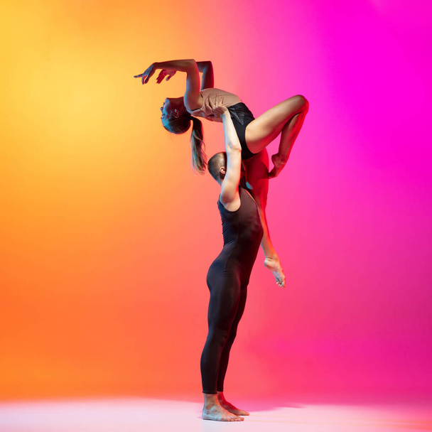 Art performance. Two dancers, stylish sportive couple, male and female models dancing contemporary dance on colorful gradient yellow pink background in neon light. - Foto, Bild
