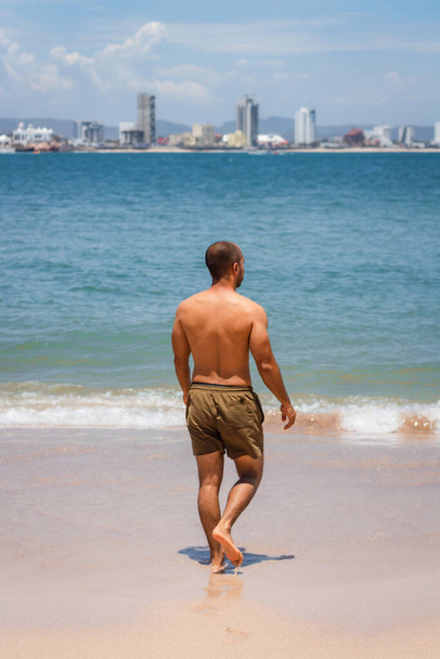 A fiatal latin férfi a tenger felé sétál vissza a kamerába - Fotó, kép