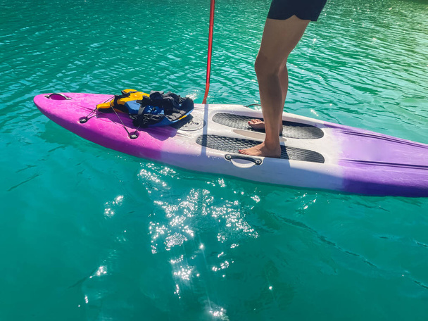 Beautiful and strong woman on a sup board and enjoying turquoise transparent water in the lake. Tropical travel, wanderlust and water activity concept. Paddle Surf water sports. Summer vacations. - 写真・画像