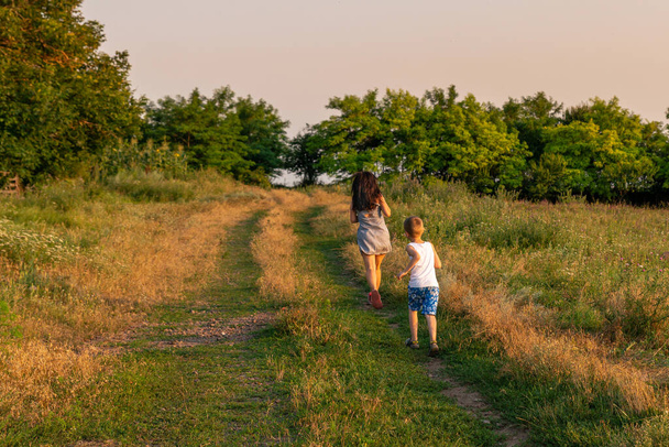 Matka i syn biegną wiejską drogą na wsi. Spacer na świeżym powietrzu na obszarach wiejskich przed zachodem słońca. - Zdjęcie, obraz