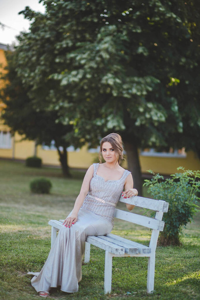 A beautiful Caucasian female from Bosnia and Herzegovina in an elegant dress sitting on a wooden bench - Zdjęcie, obraz