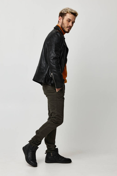 a man in a leather jacket, orange sweater and trousers turned to the side on a Light background copy Copy Space - Photo, Image