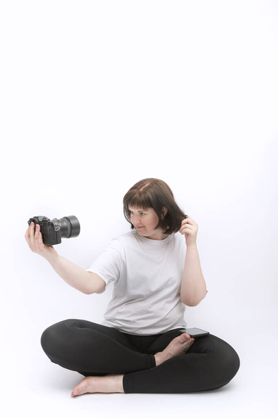 Junge Frau in Sportkleidung macht Selfie mit professioneller Kamera. Mädchen sitzt in Lotusposition und fotografiert sich selbst - Foto, Bild