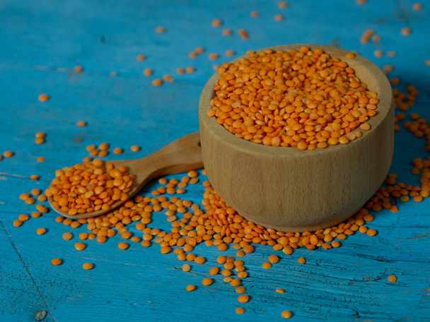 Red lentils in a wooden plate and spoon on an old rustic table. Vegetarian food. - Photo, Image