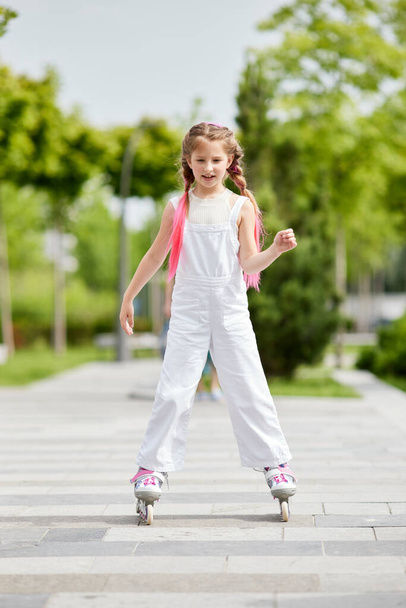 Cheerful little girl on roller skates with braided hair style - Zdjęcie, obraz