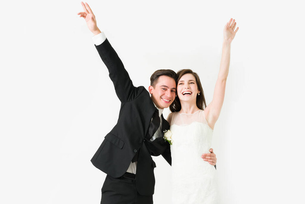 Cheerful couple laughing and raising their arms after the ceremony. Bride and groom celebrating at their wedding reception - Photo, Image
