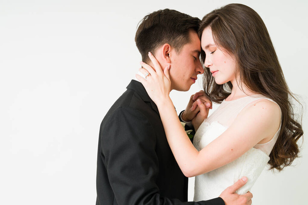Προφίλ μιας αξιολάτρευτης νεαρής νύφης και του γαμπρού που αγκαλιάζονται πρόσωπο με πρόσωπο ενώ κλείνουν τα μάτια τους για μια ρομαντική στιγμή - Φωτογραφία, εικόνα