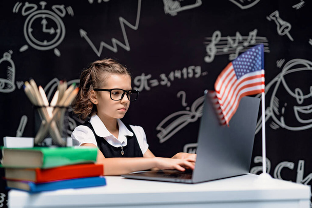 beautiful little schoolgirl at desk against black background with USA flag - Photo, Image