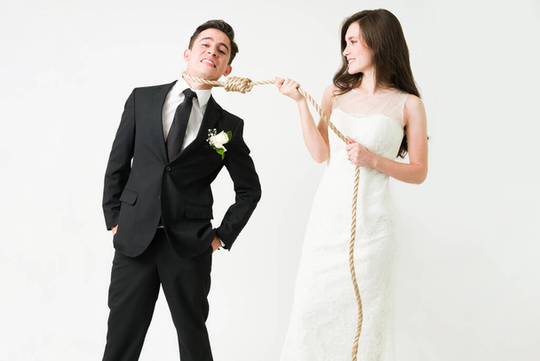 Je zult altijd bij me zijn. Een gestresste bruidegom die naar de camera kijkt terwijl haar vrouw een touw om zijn nek wikkelt om te trouwen.  - Foto, afbeelding