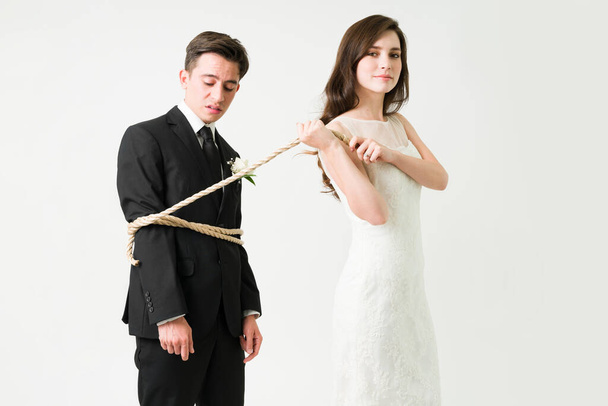 Attractive bride-to-be pulling her husband with a rope and forcing him to get married on their wedding day - Foto, Imagem
