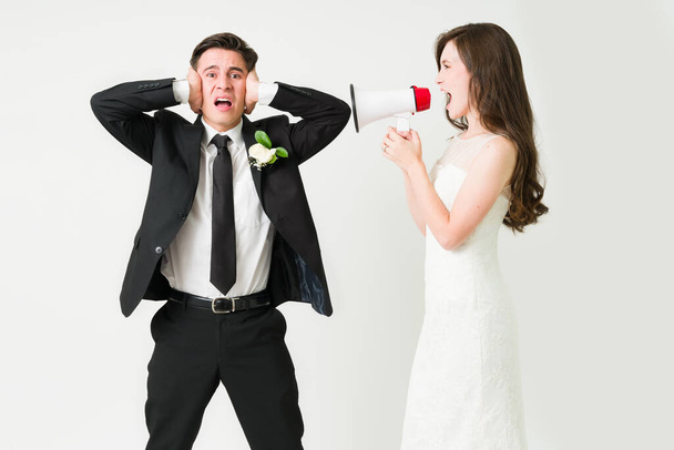 Bossy junge Braut hält ein Megafon und schreit ihren Mann an ihrem Hochzeitstag an  - Foto, Bild