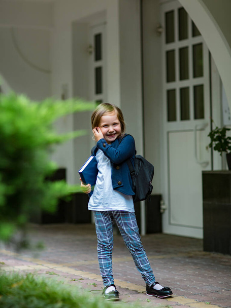 красивая маленькая девочка, школьница, во второй половине дня возле школы, в стильной школьной форме - Фото, изображение
