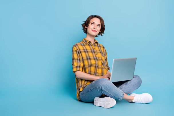 Fénykép álmodozó kíváncsi hölgy ül padló munka netbook néz üres tér kopás kockás ing elszigetelt kék szín háttér - Fotó, kép