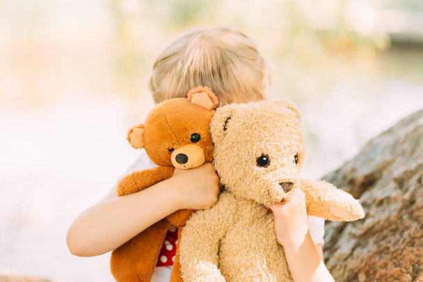 Little girl blonde hugs a soft toy bear. - Фото, изображение