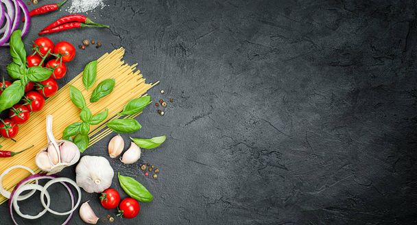 cherry tomatoes, pasta, basil, garlic, onion, chili and peppercorns on a black concrete table, ingredients for making pasta - Photo, Image