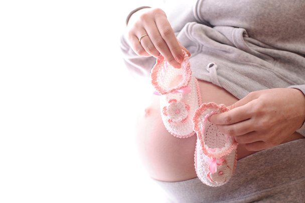 Belly of expectant mother with pink baby's bootee isolated on white - Foto, Imagem