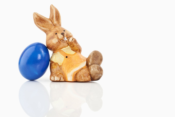 Um coelho da Páscoa está sentado ao lado de um ovo colorido
 - Foto, Imagem