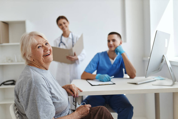 Χαρούμενη ηλικιωμένη γυναίκα στο ραντεβού με γιατρούς και νοσηλευτές στο νοσοκομείο - Φωτογραφία, εικόνα