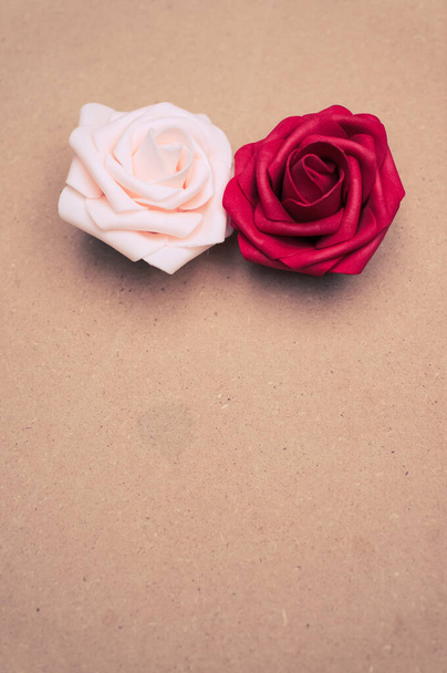 A vertical closeup of two artificial roses on the brown background. - Zdjęcie, obraz