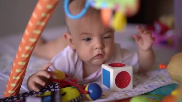 Bambino si trova sulla sua pancia su un tappeto da gioco e gioca con i giocattoli - Filmati, video