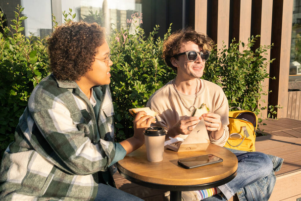 Dos adolescentes felices tomando bocadillos y tomando café afuera - Foto, imagen