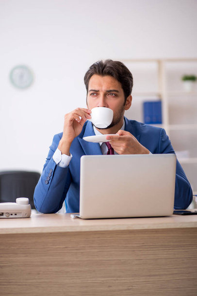 Jonge mannelijke werknemer die koffie drinkt tijdens de pauze - Foto, afbeelding