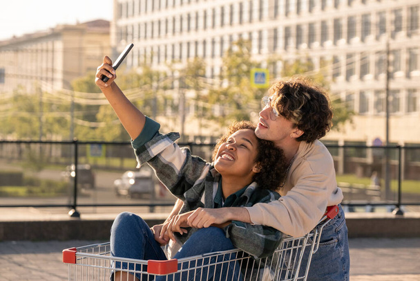 Two happy millennials making selfie in urban environment - Фото, изображение