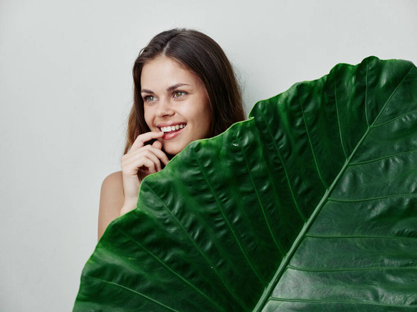 χαμογελαστή γυναίκα με ένα μεγάλο πράσινο φύλλο σε ένα ελαφρύ εξωτικό φόντο - Φωτογραφία, εικόνα