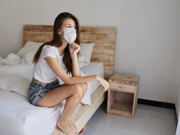 kobieta na wakacjach siedzi na łóżku w hotelowej masce medycznej na pandemii kwarantanny twarzy - Zdjęcie, obraz