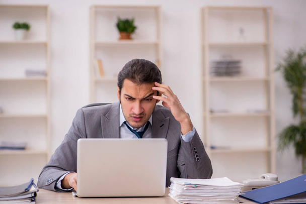 Молодой работник мужчина недоволен чрезмерной работой в офисе - Фото, изображение