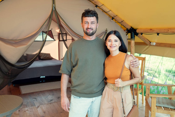 Happy young man and woman standing against interior of their glamping house - Photo, Image