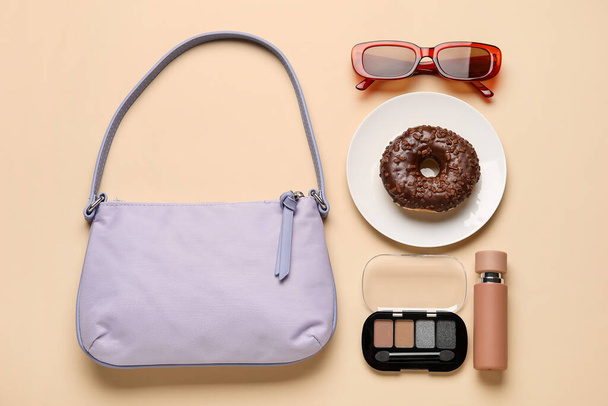 Skład z modnej torebki, talerz z pączkiem i akcesoria na tle koloru - Zdjęcie, obraz