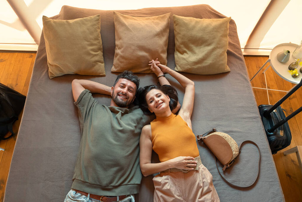 Современная молодая пара, держащаяся за руки, лежа на кровати - Фото, изображение